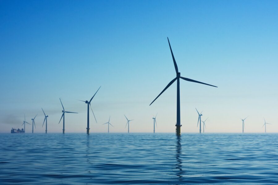 Photo of an offshore wind farm with at least 12 large, three-bladed wind turbines rising up from the ocean